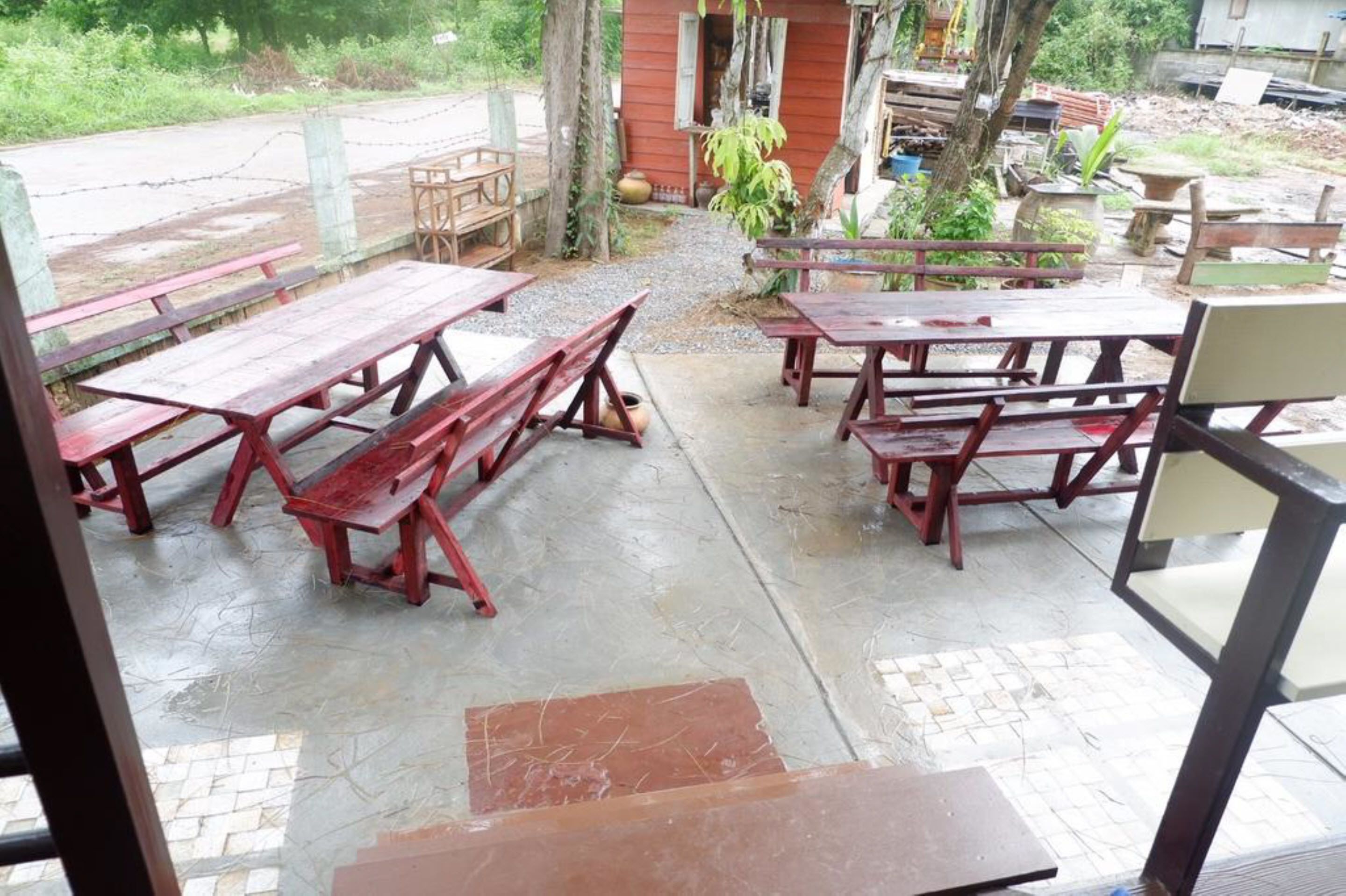 Un espace extérieur aménagé avec plusieurs tables et bancs de pique-nique en bois, un sol en béton et une vue sur une route et la verdure en arrière-plan.