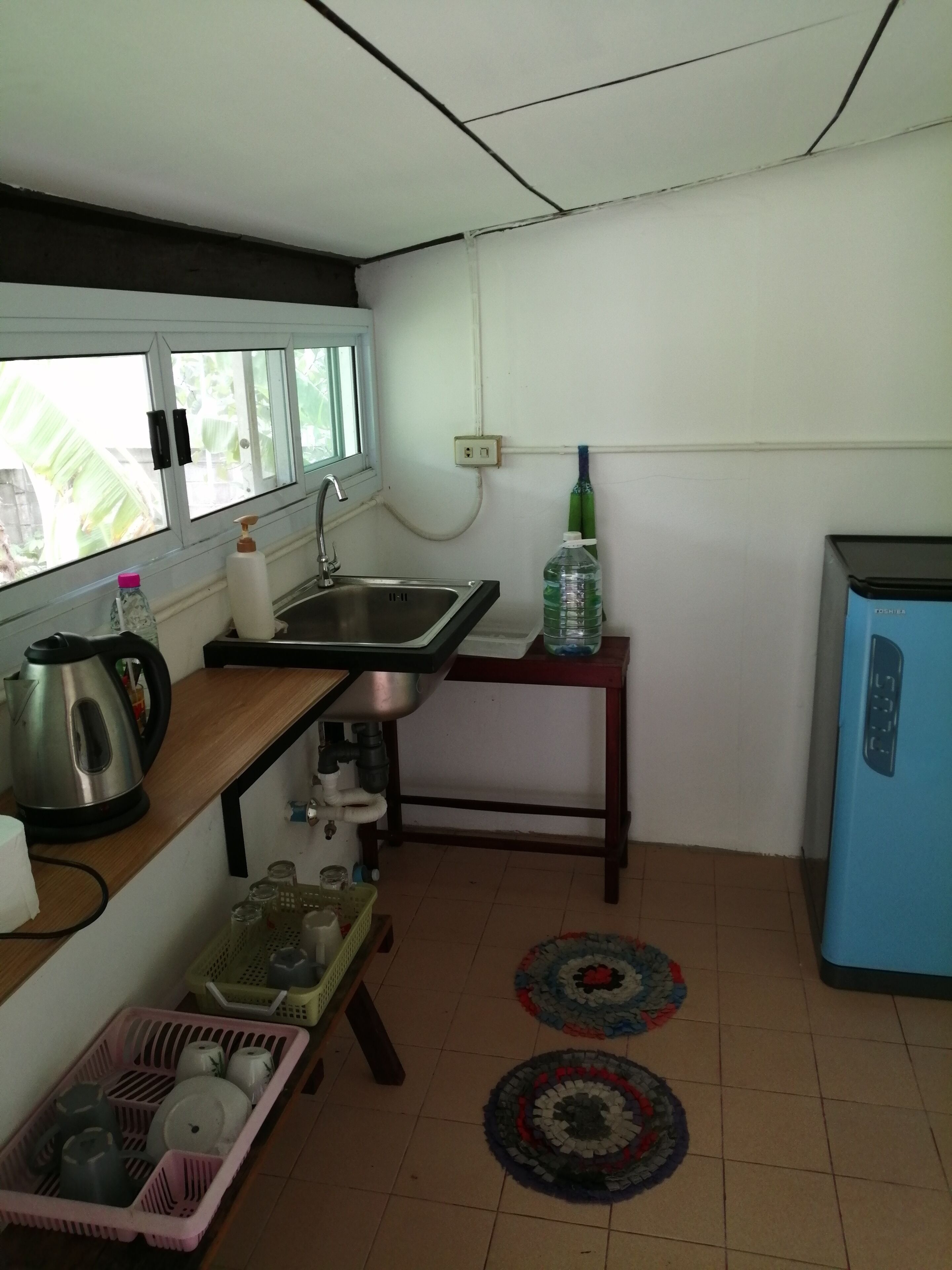 Cucina con lavello, bollitore, frigorifero e finestra vista su spazi verdi.