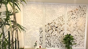 A dining area with a table set for four, white chairs, a decorative white partition with floral patterns, and two potted plants. - Tea Leaf Hotel (Cam Ly - Da Lat)