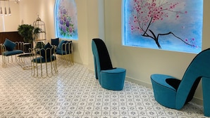 A modern lounge area with teal chairs, a patterned floor, and two large windows with floral artwork. - Tea Leaf Hotel (Cam Ly - Da Lat)