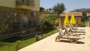 A building with a stone facade, a balcony with a wrought iron railing, and a pool area with sun loungers and yellow umbrellas. - Ada Apart Hotel (Ortaca)