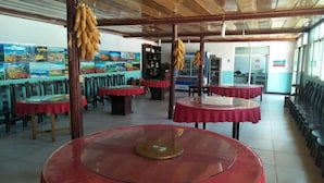 Un restaurant avec des tables rondes, des chaises et des grappes de bananes suspendues au plafond.