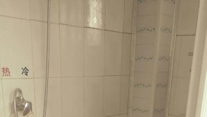 Une petite salle de bain carrelée, équipée d’une douche, de toilettes et d’un lavabo.