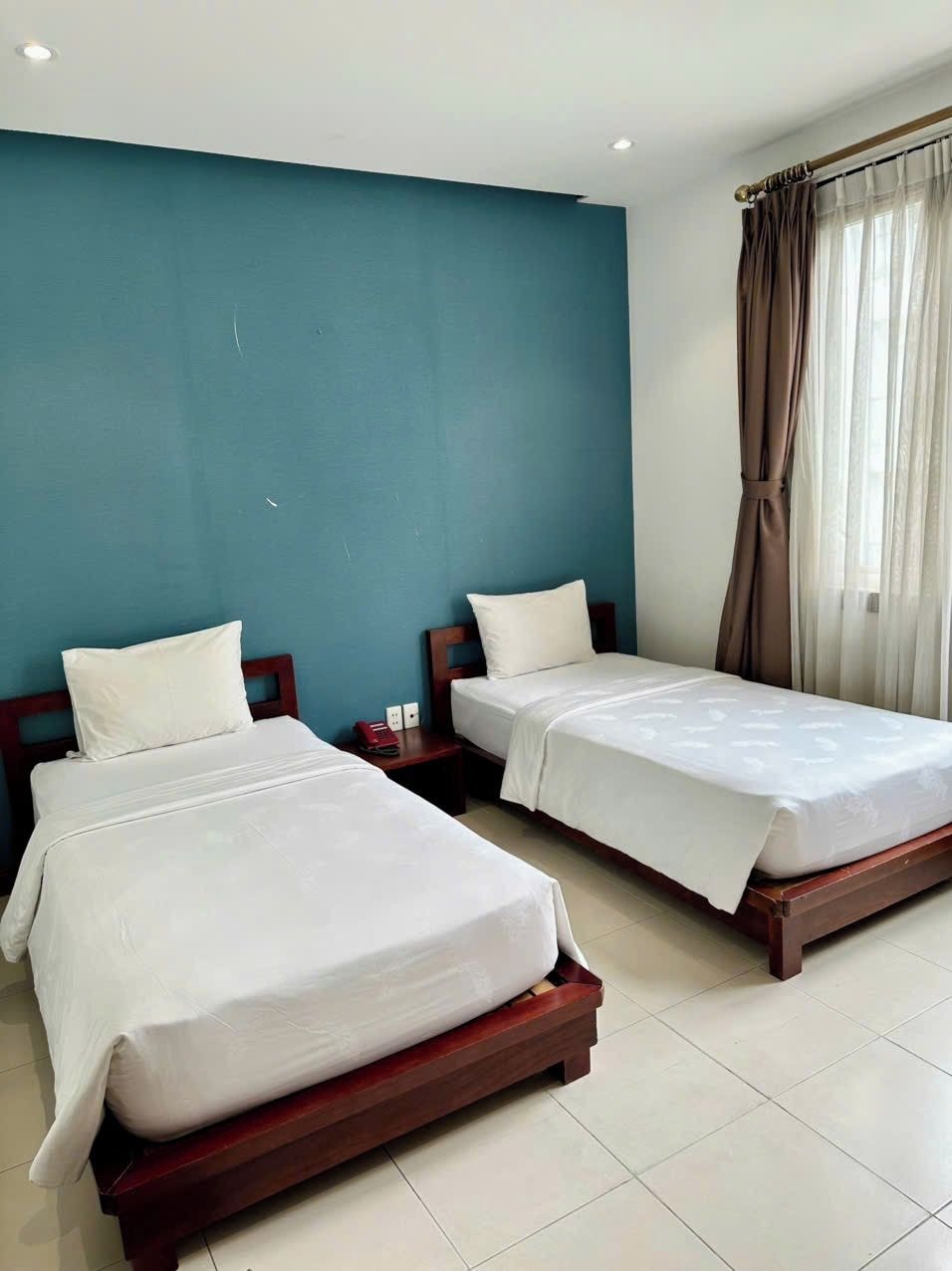 A hotel room with two single beds, a nightstand, a telephone, and a window with curtains.