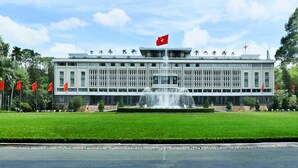Un grand bâtiment doté d’une fontaine centrale, entouré d’une pelouse bien entretenue et de drapeaux rouges.