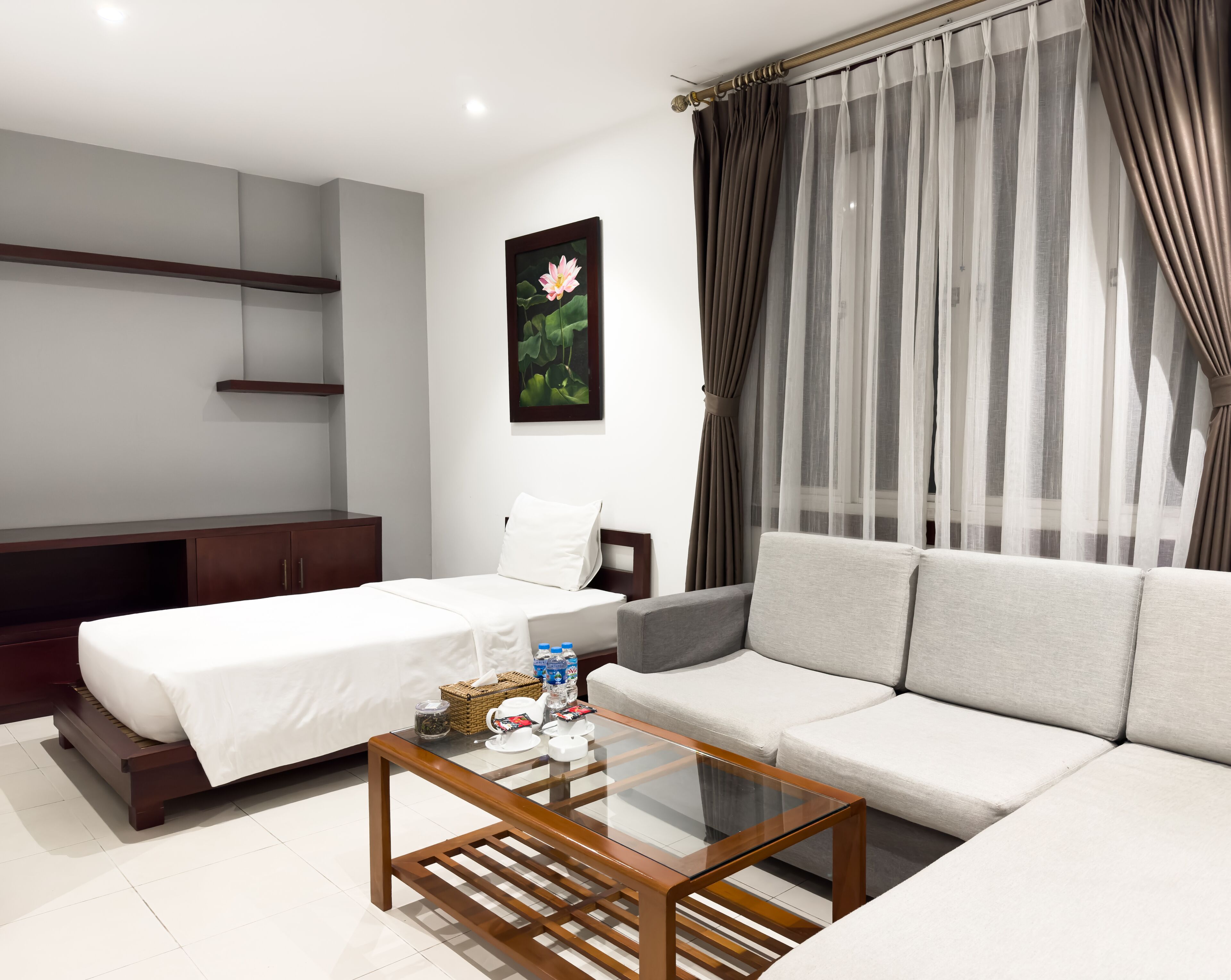A modern hotel room with a bed, sofa, and a glass coffee table.