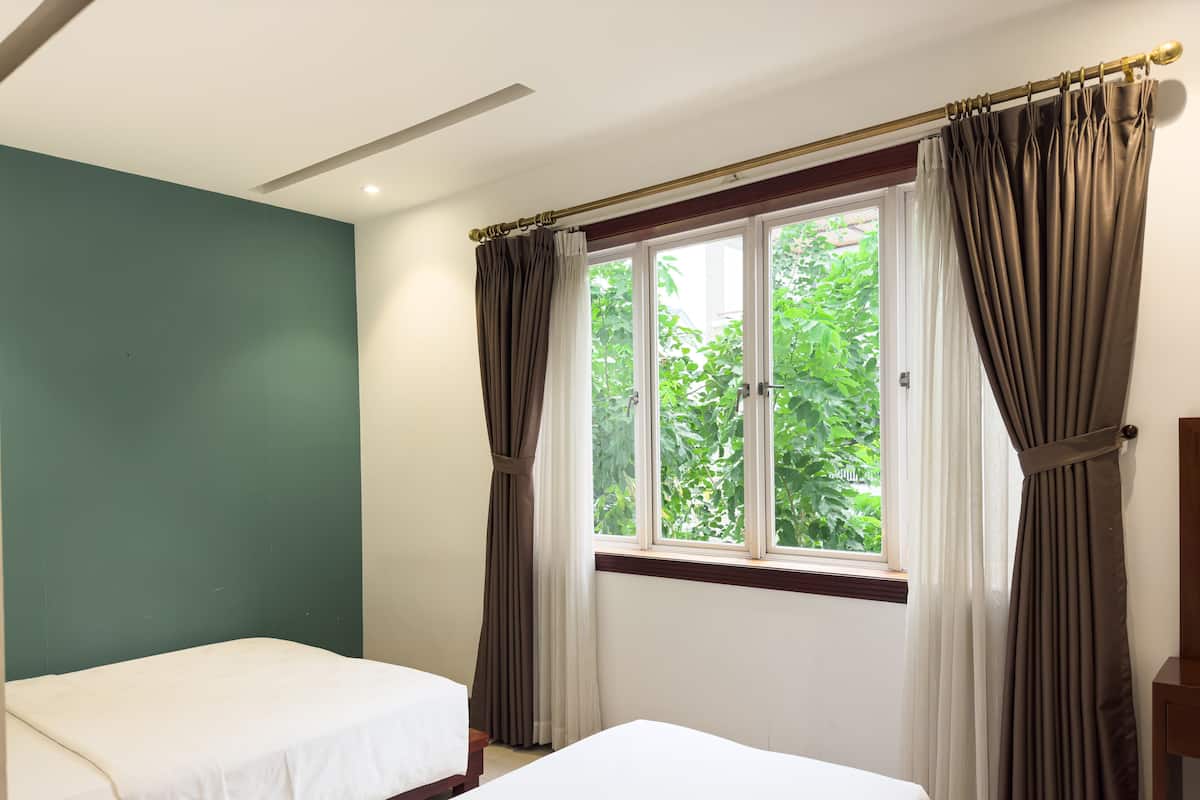 Una habitación con dos camas, una ventana con cortinas y una pared verde.