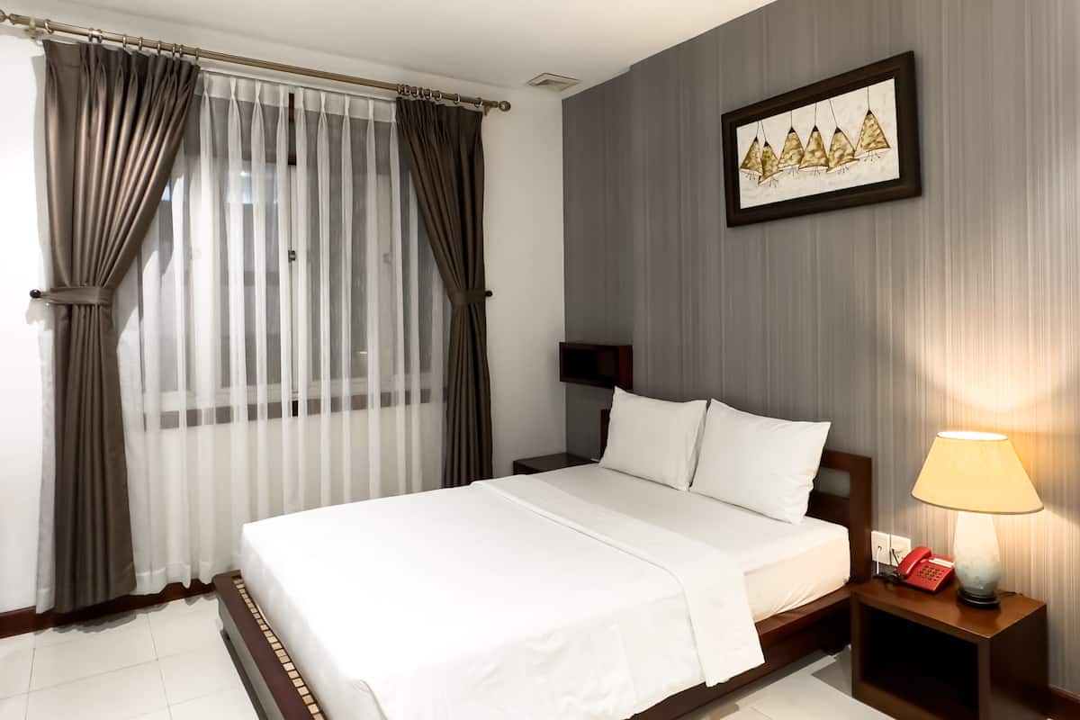 Una habitación de hotel con cama, mesita de noche con lámpara, teléfono y un cuadro en la pared.