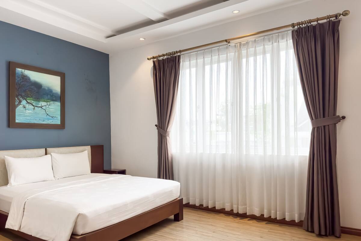 Una cama bien hecha con sábanas blancas, un cabecero de madera y un cuadro de un paisaje en la pared.