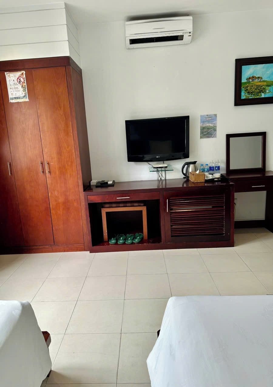 Habitación de hotel con armario de madera, televisor de pantalla plana, un mueble pequeño con hervidor y una cama con cubrecama blanco.