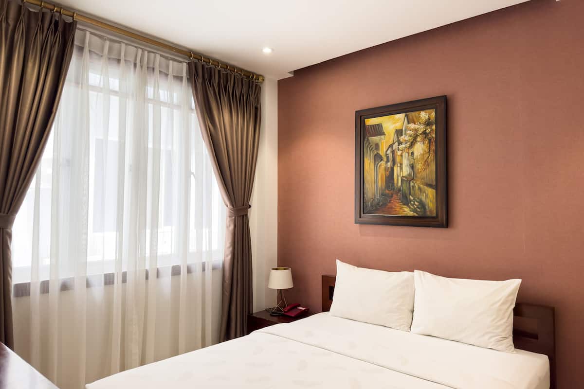 Una habitación de hotel con cama, un cuadro en la pared y una ventana con cortinas.