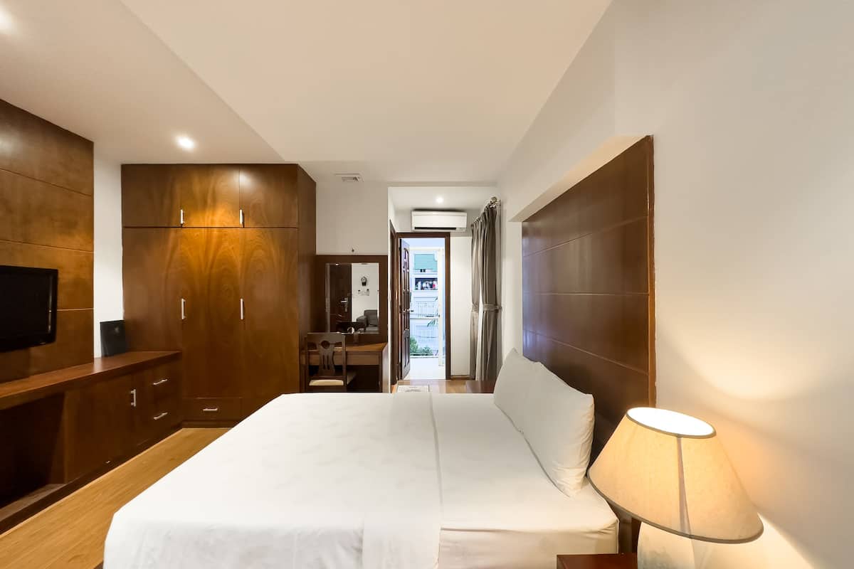 Una habitación de hotel moderna con una cama grande, un armario de madera y un televisor en la pared izquierda.