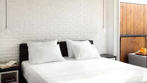 Un dormitorio moderno con pared de ladrillo blanco, cabecero negro y suelo de madera. Hay una mesita de noche con un libro y una lámpara.
