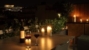 Una mesa con una botella de vino y dos copas, rodeada de velas, con vistas a un edificio al fondo.