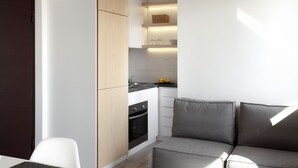 Uma cozinha compacta com eletrodomésticos embutidos, um espaço de refeições com mesa e cadeiras, e um sofá com almofadas.
