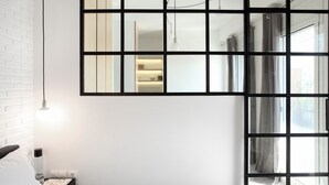 Quarto de hotel moderno com uma janela grande, uma cama, uma mesa de cabeceira e um espelho fixado na parede.