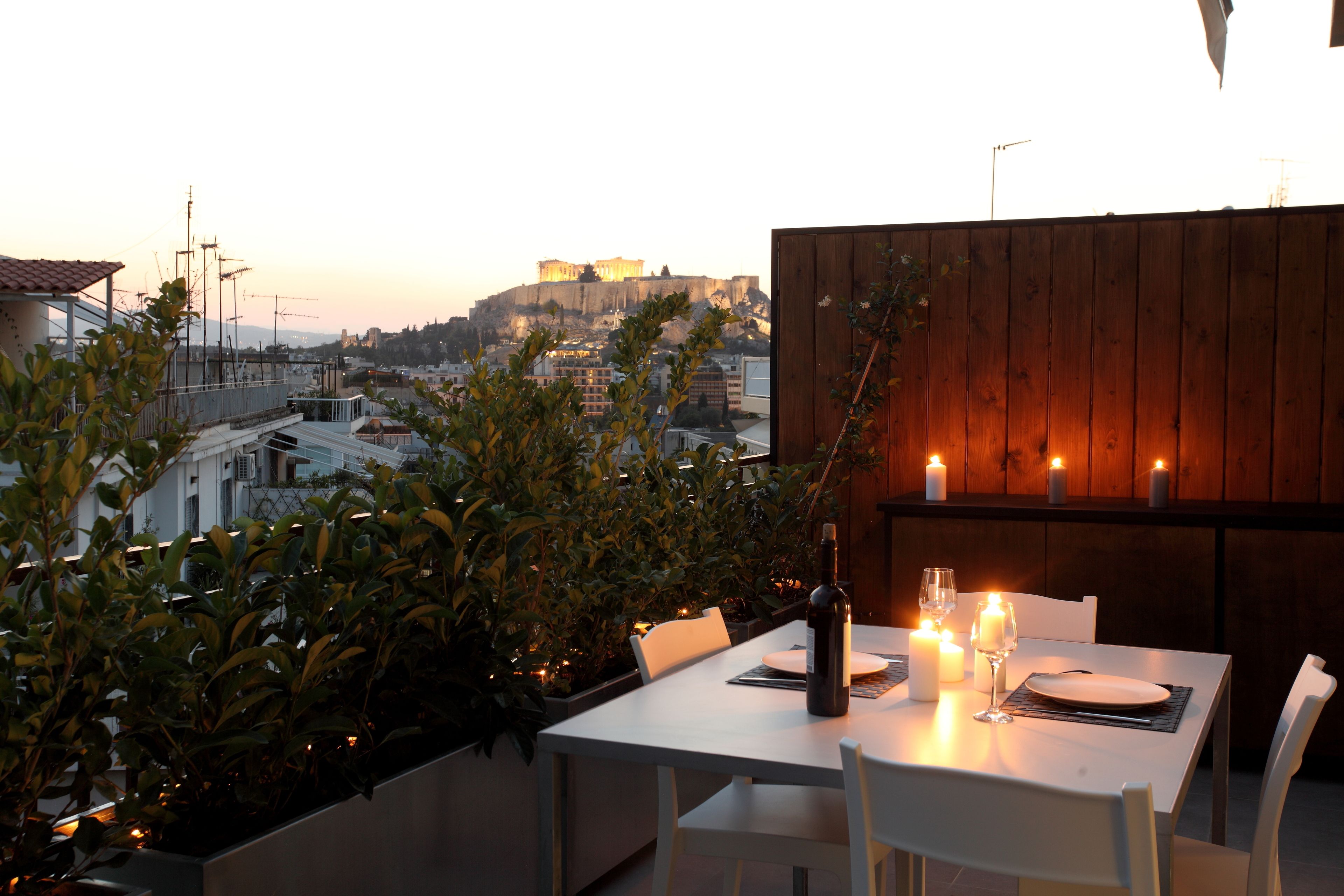 Uma área de refeições ao ar livre com uma mesa posta para dois, com vista para uma paisagem urbana e um edifício imponente ao longe.
