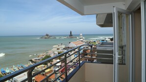 A balcony with a view of the sea, buildings, and a lighthouse. - Hotel Maadhini (Nagercoil)