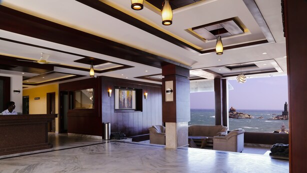 A hotel lobby with a marble floor, a reception desk, seating area, and a view of the sea. - Hotel Maadhini (Nagercoil)