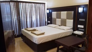 A hotel room with a large bed, a bedside table, and a nightstand. - Hotel Maadhini (Nagercoil)