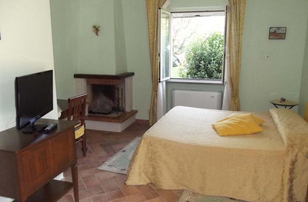Quarto com cama, televisão em cómoda de madeira, lareira e janela com cortinas.