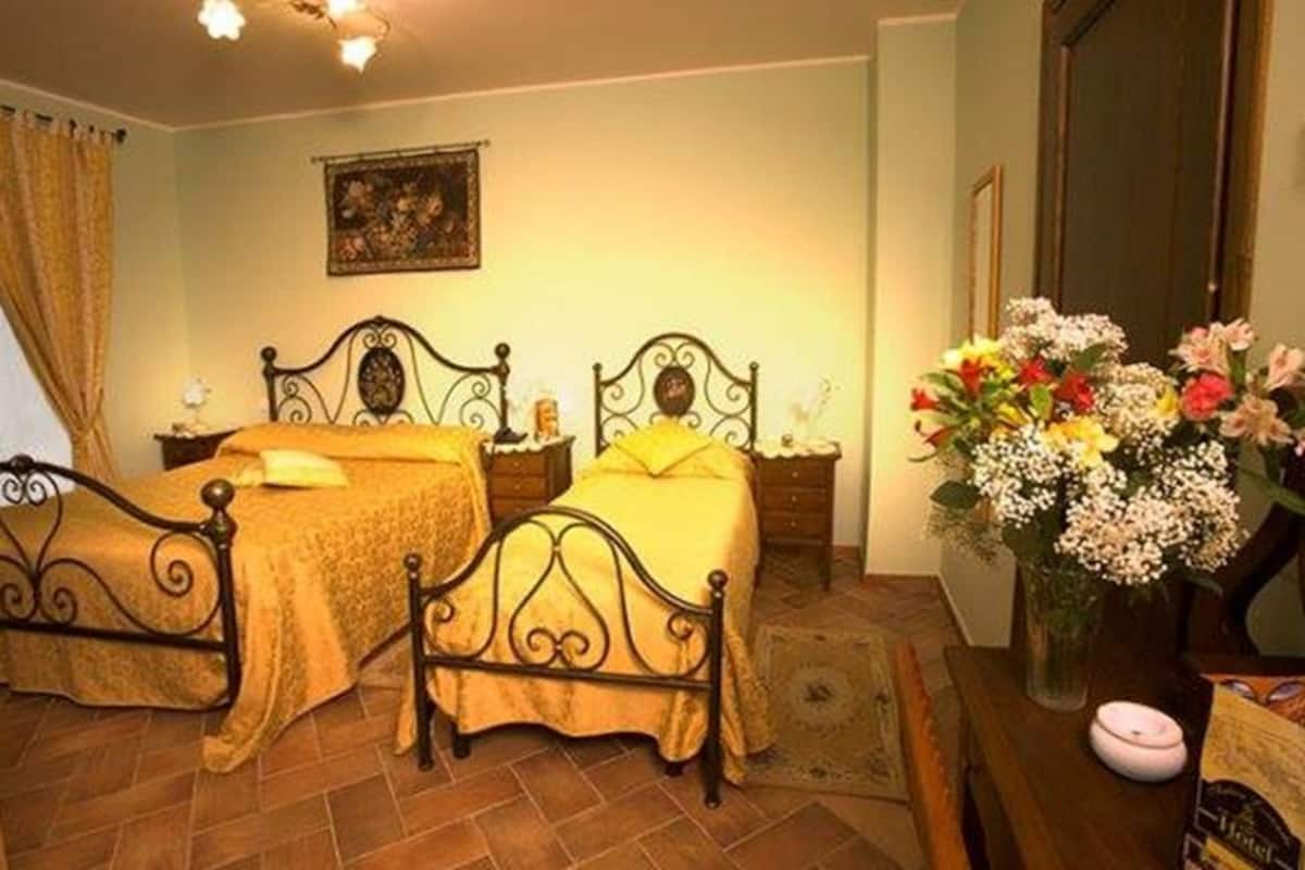 A room with two beds, a wooden dresser, a vase with flowers, and a painting on the wall.
