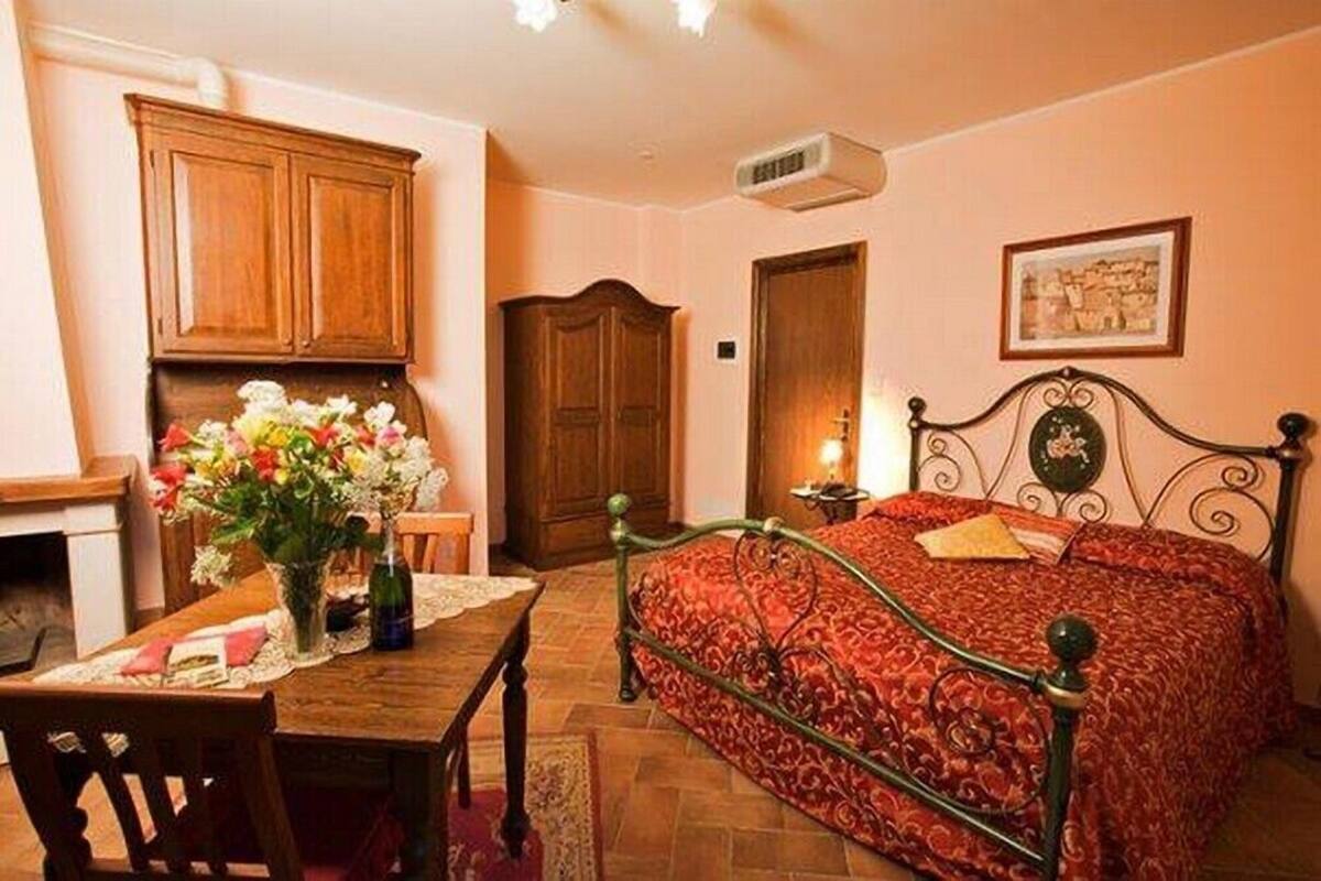 A bedroom with a bed, a wooden cabinet, a table with a vase of flowers, and a framed picture on the wall.