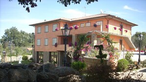 Un immeuble de deux étages avec une façade en pierre, de nombreuses fenêtres et un balcon orné de plantes en suspension.