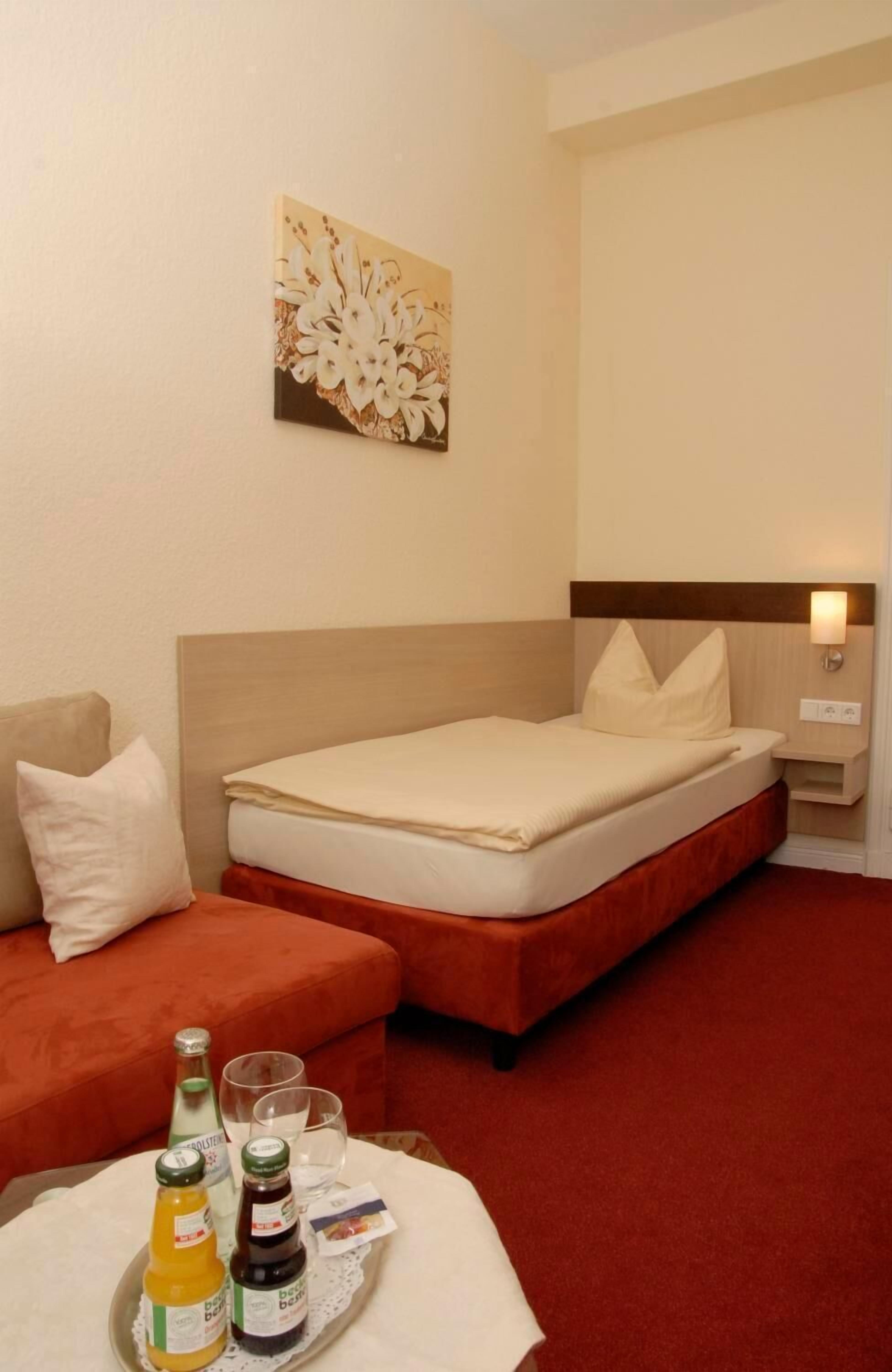 Una habitación de hotel con una cama, una mesita con bebidas, un sofá y un cuadro en la pared.