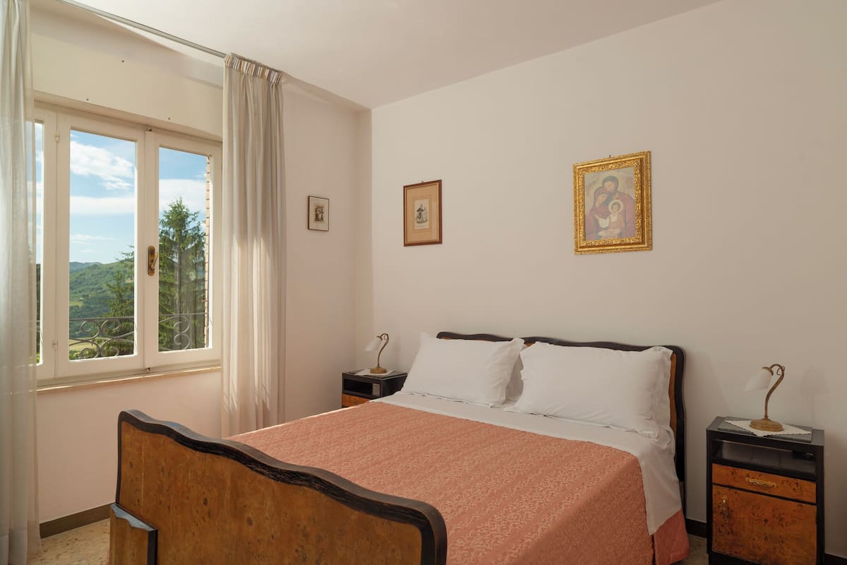 Une chambre à coucher avec un lit, une table de chevet, une fenêtre avec des rideaux et deux tableaux encadrés accrochés au mur.
