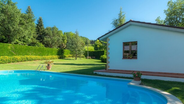 A swimming pool with a clear blue water, surrounded by a well-maintained lawn and trees. - Lucrezia e Cesare Borgia (Serrapetrona)