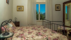 A bedroom with a bed, a nightstand, a lamp, a chair, and a window with curtains. - Lucrezia e Cesare Borgia (Serrapetrona)