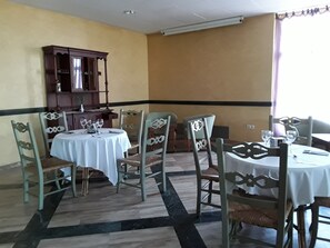 Un coin repas comprenant une table ronde, des chaises, un buffet en bois et une fenêtre avec des rideaux.