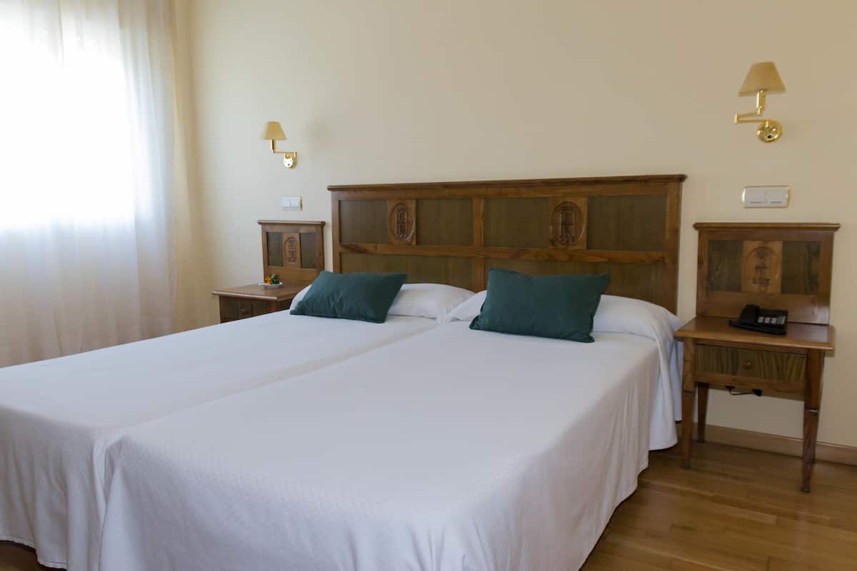 Ein Hotelzimmer mit zwei Betten, Holz-Kopfteilen, Nachttischen mit Lampen und einem Holzbeistelltisch mit Telefon.
