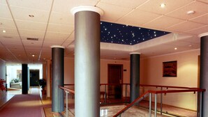 A hotel corridor with a starry ceiling, large pillars, and a wooden floor. - Hotel ELE Puerta de Monfragüe (Malpartida de Plasencia)