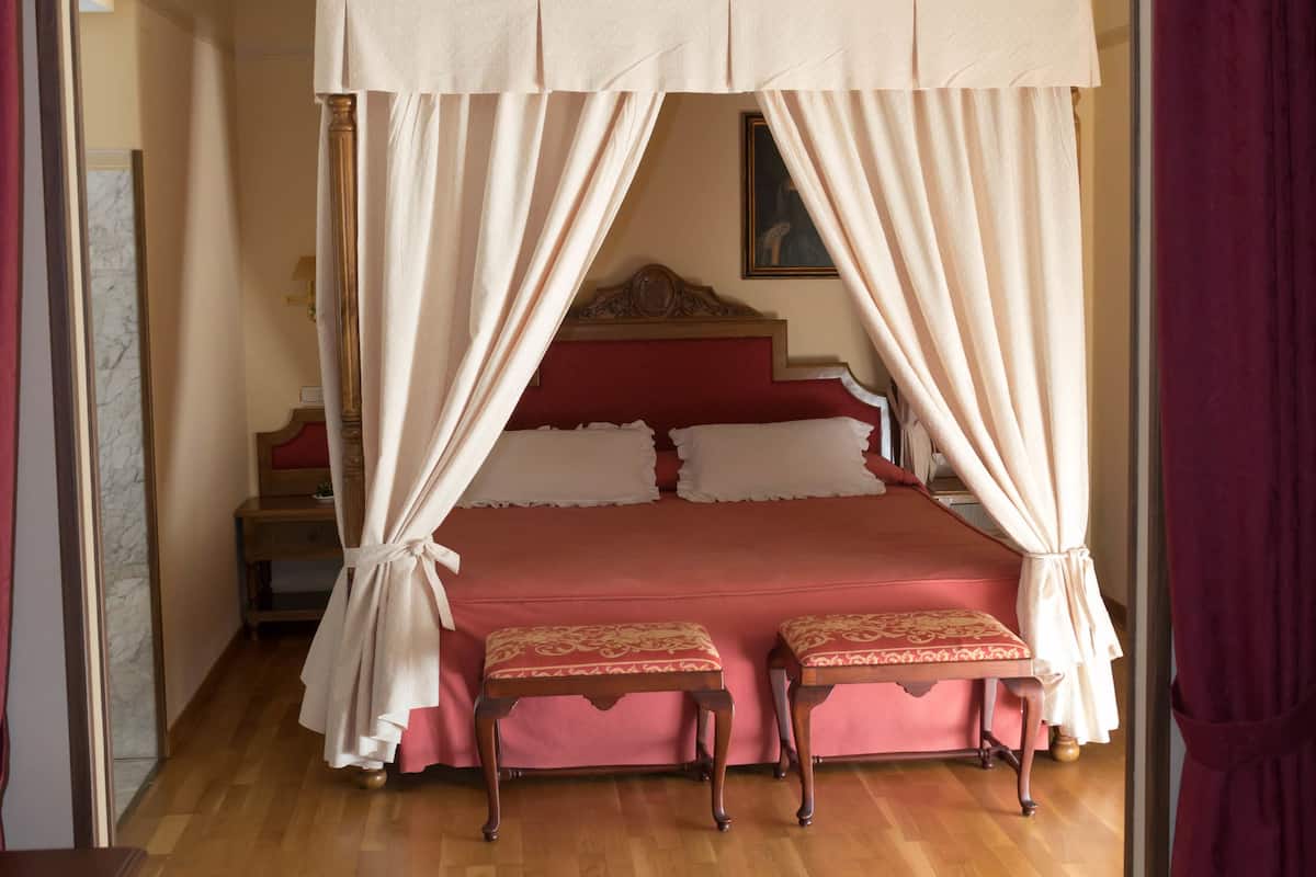 Ein Schlafzimmer mit einem Himmelbett, einem Nachttisch aus Holz und einer Bank.