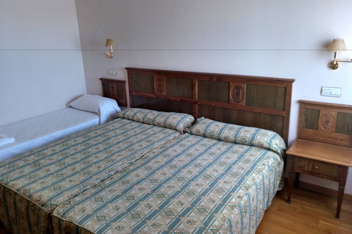 Ein Schlafzimmer mit einem großen Bett, einem kleineren Bett, einem Holzkopfstück, Nachttischen und Wandlampen.