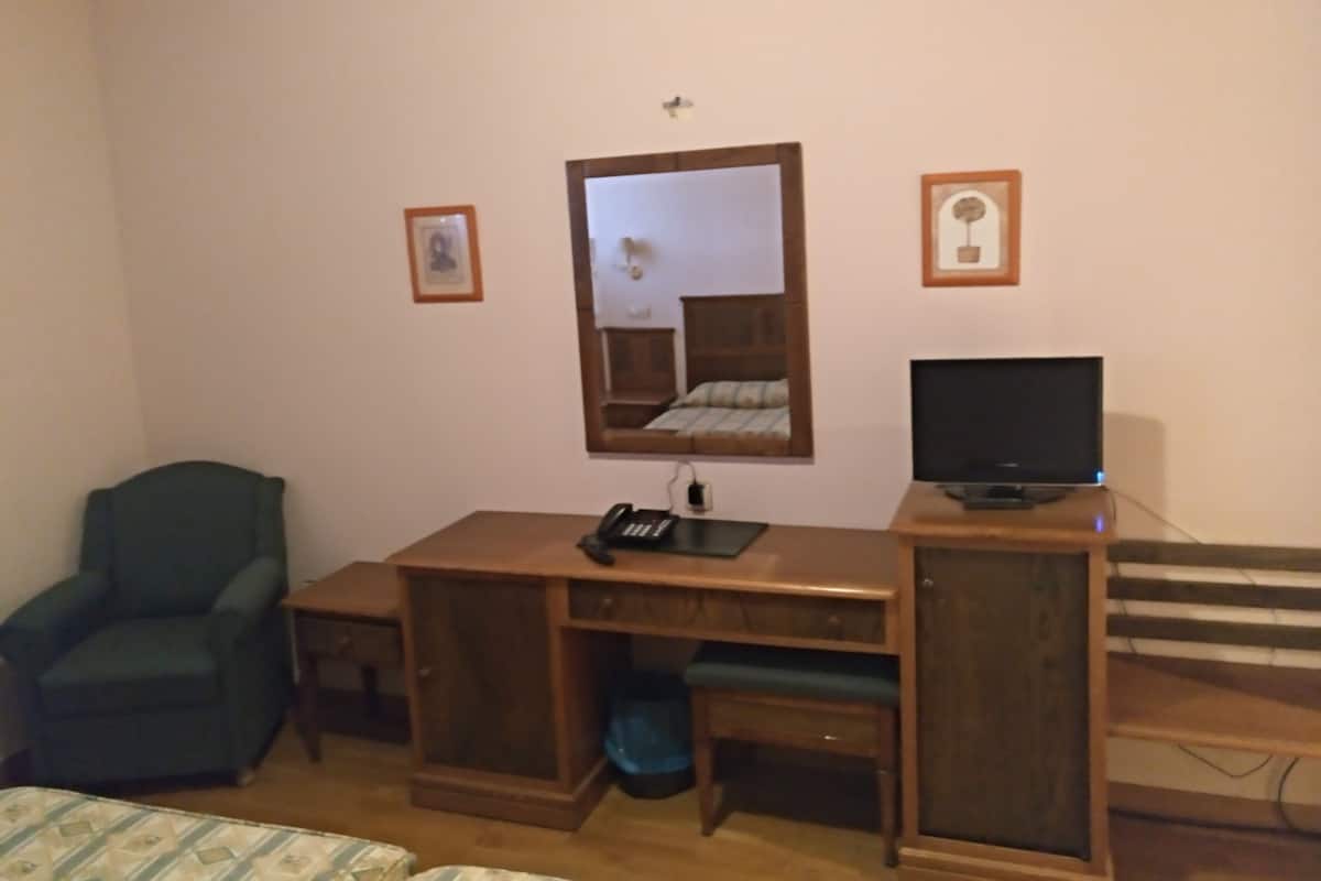 Ein Schlafzimmer mit einem Bett, einem Schreibtisch mit Computer, einem Stuhl und einem Spiegel.