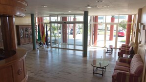 A spacious lobby with a wooden reception desk, a glass coffee table, and striped sofas. - Hotel ELE Puerta de Monfragüe (Malpartida de Plasencia)