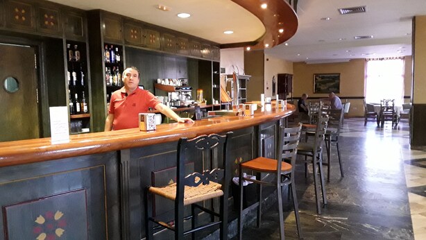 A bar area with a bartender, bar stools, and a counter with various items. - Hotel ELE Puerta de Monfragüe (Malpartida de Plasencia)