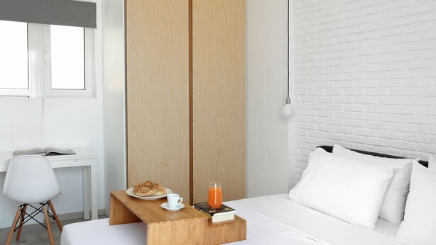 A modern hotel room with a wooden bedside table, a bed with white bedding, a white chair, and a brick-patterned wall. - Athens View Loft - 04 (Athens)