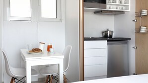 A compact kitchenette with a microwave, stove, and storage shelves. There is a small dining table with chairs and a breakfast setup. - Athens View Loft - 04 (Athens)