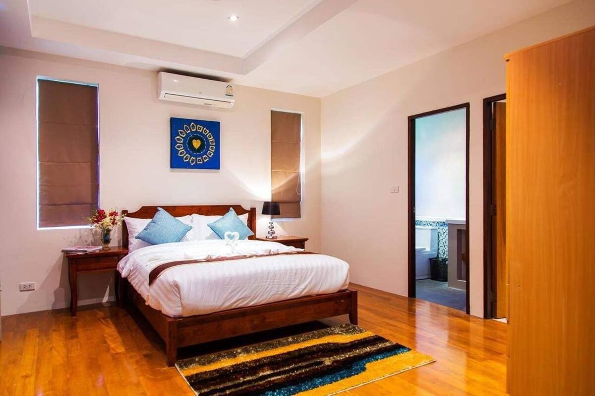 A bedroom with a wooden bed, a nightstand, a wall-mounted air conditioner, and a window with blinds.