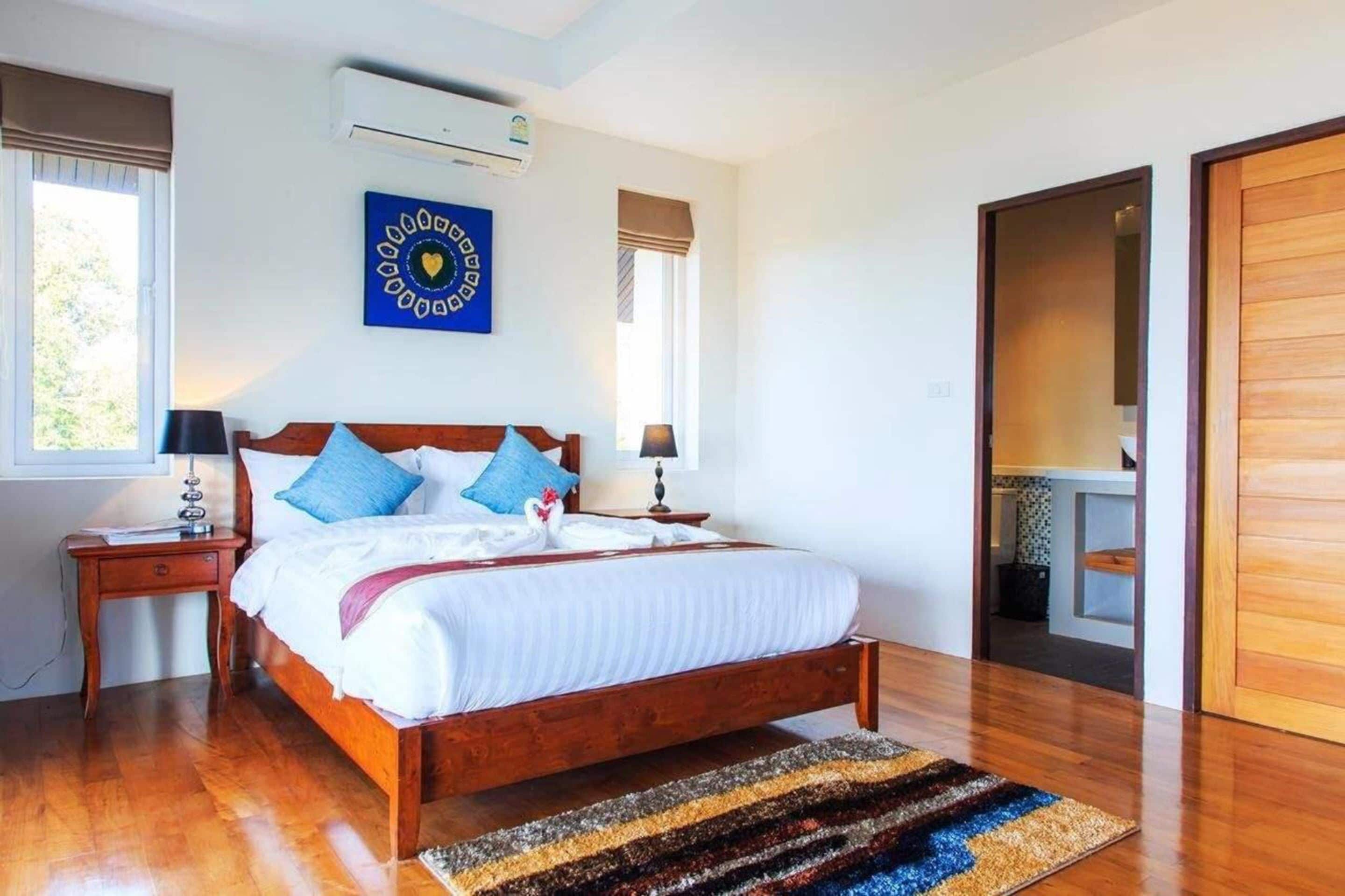 A bedroom with a wooden bed, two bedside tables, a wall-mounted air conditioner, and a large mirror.