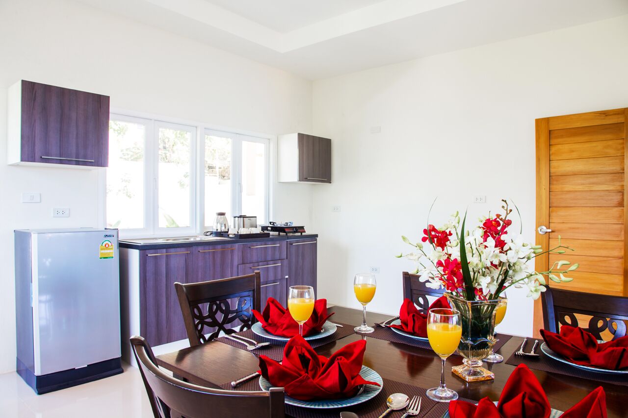A modern kitchen with a refrigerator, cabinets, and a dining area set for breakfast with orange juice and flowers.