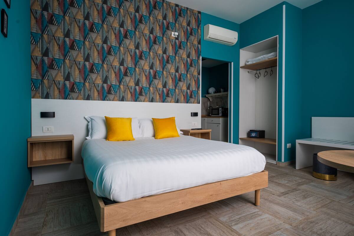 A modern bedroom with a wooden bed, two yellow pillows, a geometric patterned wall, a built-in wardrobe, and a small round table.