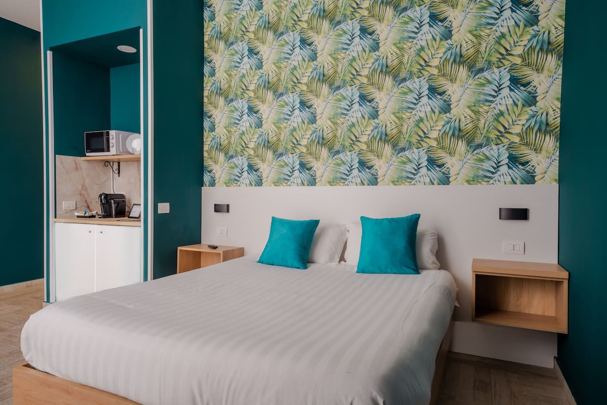 A modern bedroom with a large bed, teal walls, a leaf-patterned wallpaper, and built-in shelves.