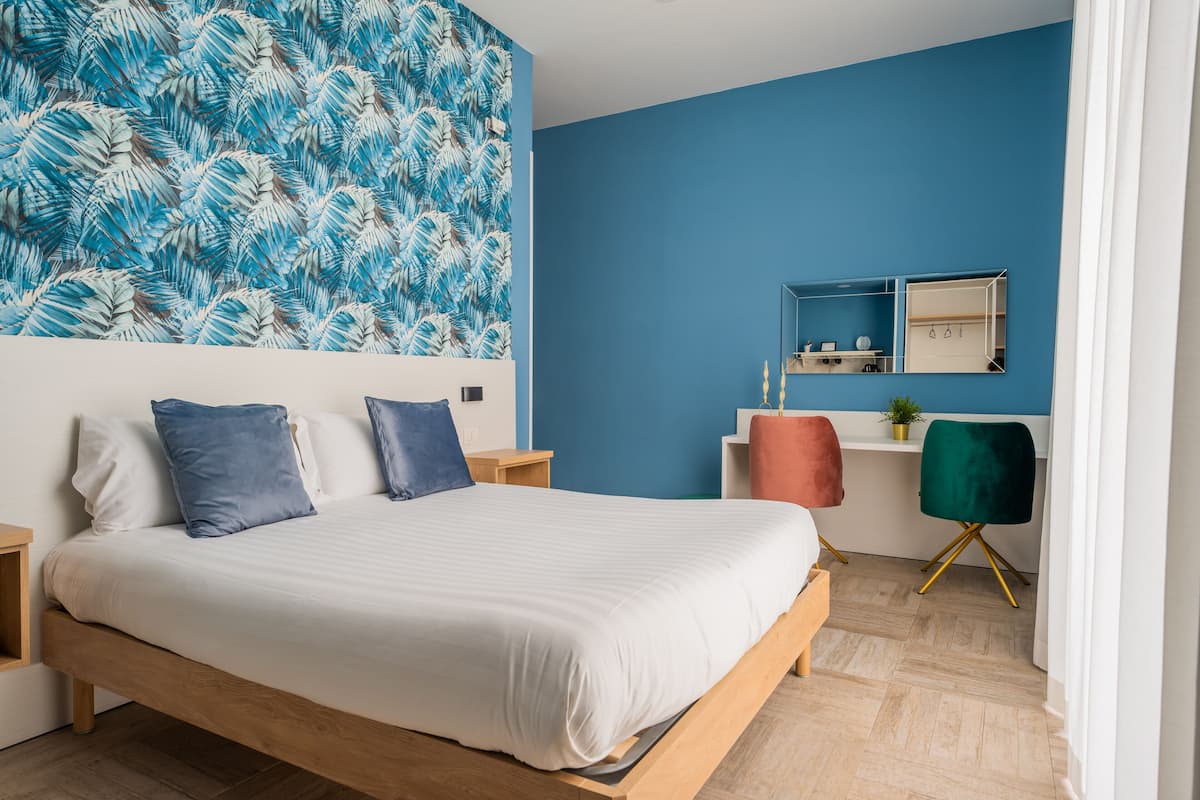 A modern bedroom with a large bed, a blue accent wall, a mirror, and a desk with a chair.