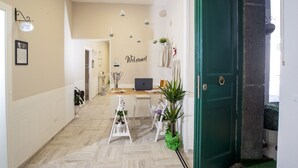 A hallway with a wooden floor, a green door, a laptop on a table, and potted plants. - B&B Pontenuovo Bed (Naples)