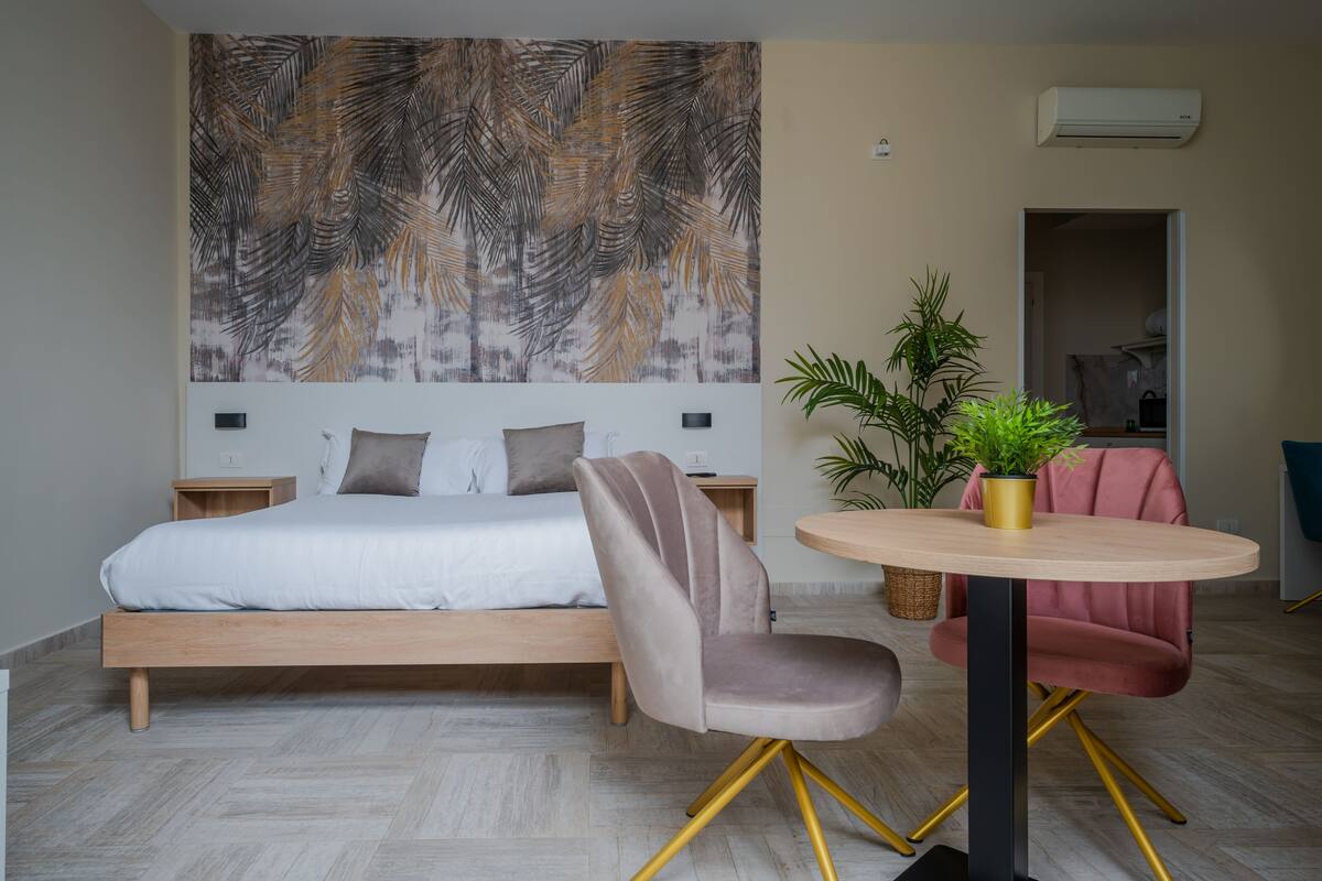 A bedroom with a bed, a chair, a round table, and a wall with a leaf pattern.